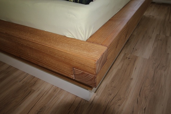 Massives Holzbett mit sichtbarer Maserung steht auf Laminatboden im modernen Schlafzimmer.