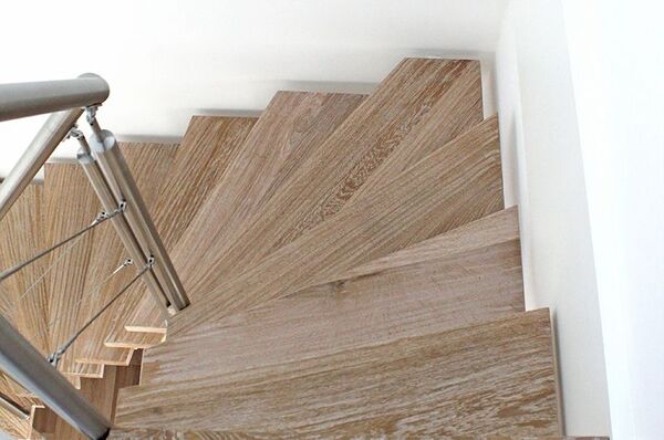 Moderne Holztreppe mit Edelstahngeländer und elegantem Design in heller Wohnumgebung.